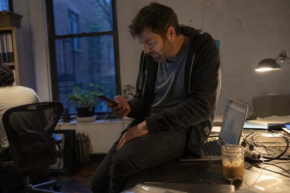 Founder checking a pricing change alert on his phone at his desk in the evening